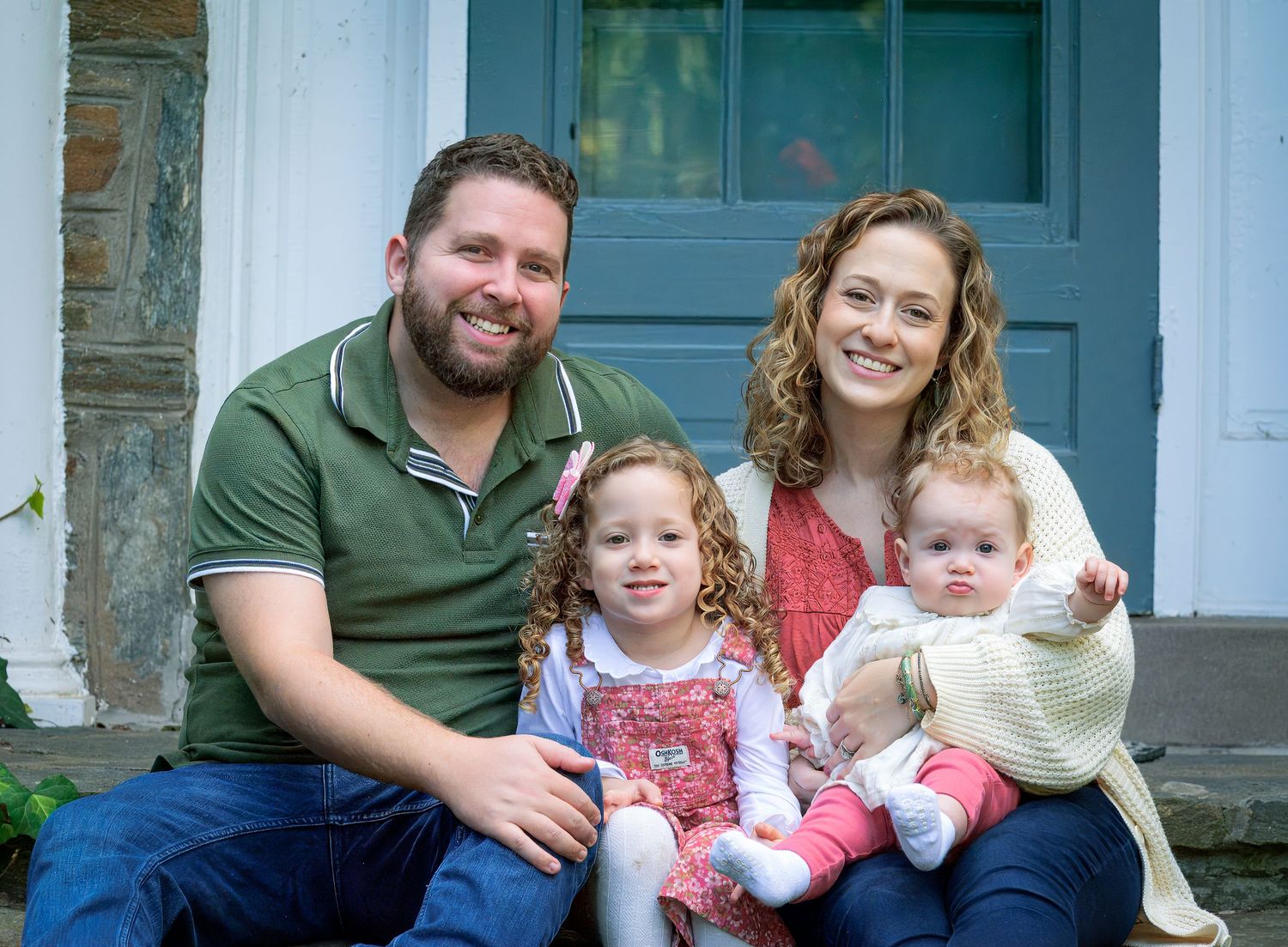 A family of four sitting together on their front porch steps with a blue door in the background.