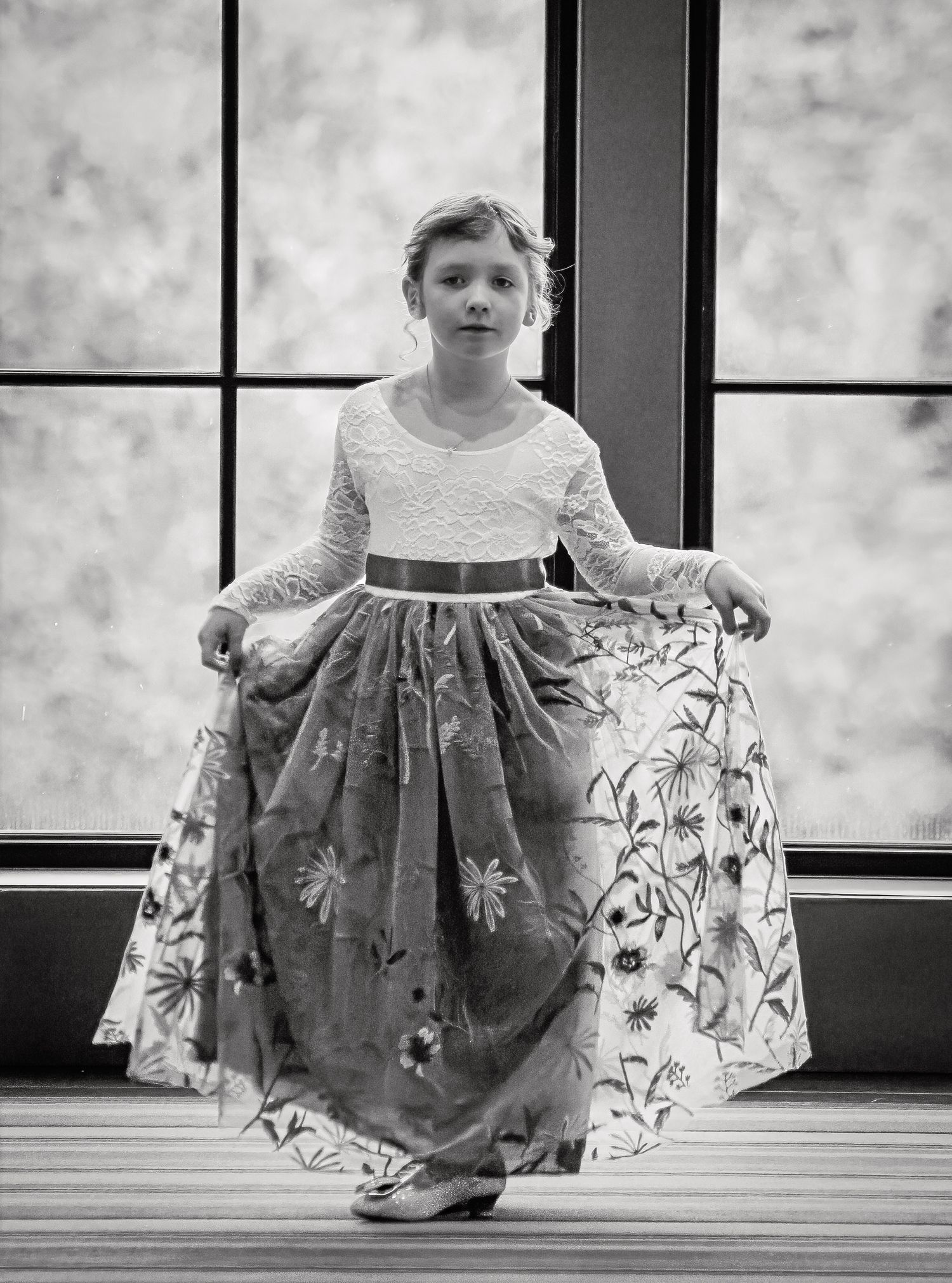 A series of black and white photos showing a small child in a floral dress twirling and playing in front of windows.