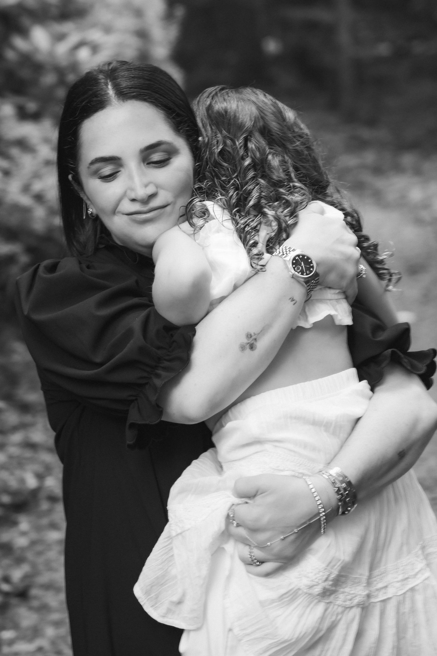 Black and white photo of a woman tenderly hugging a young girl in a white dress outdoors.