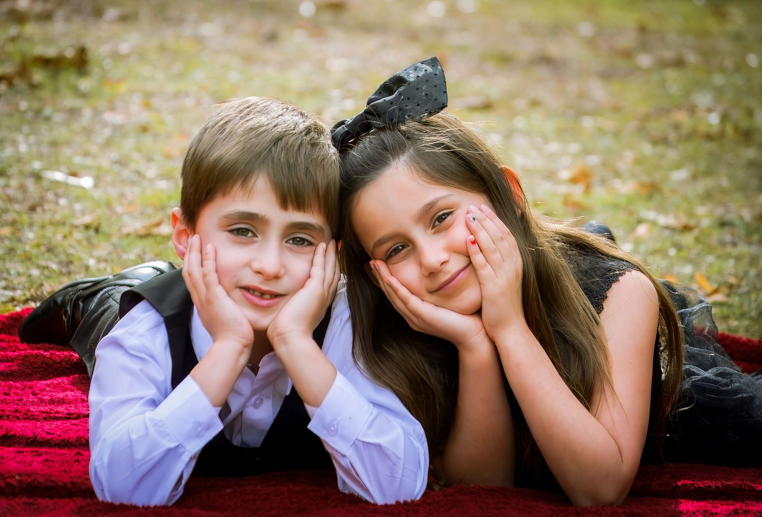 A playful series of children lying on a red blanket outdoors taking casual portraits.