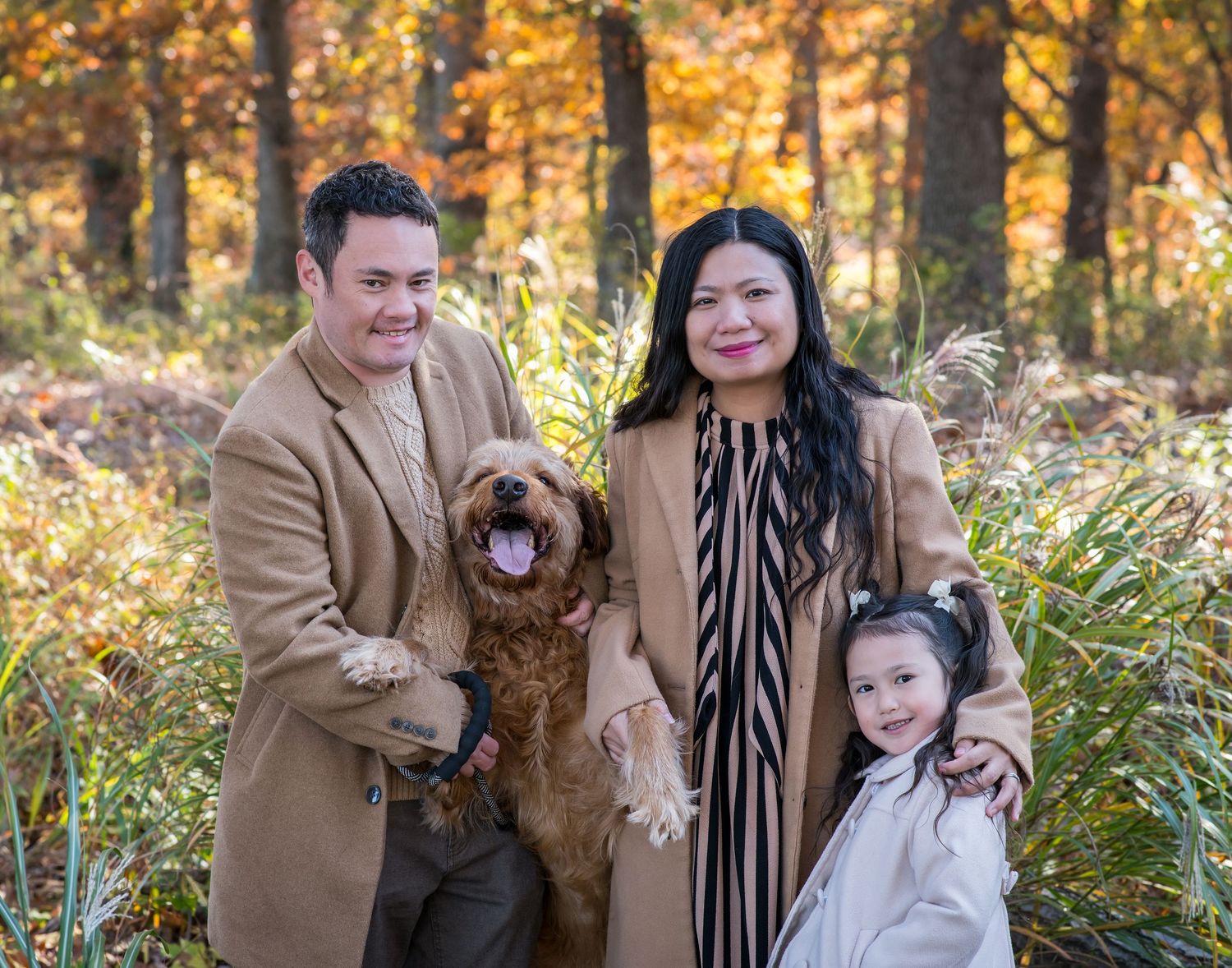 Family and their golden retriever dog pose together in autumn forest with golden foliage in background.