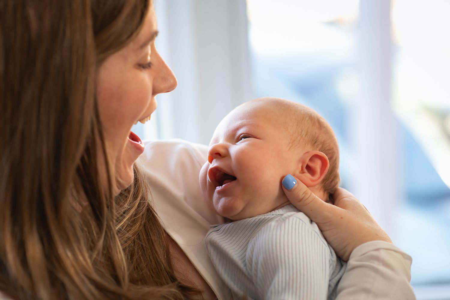 A tender moment between parent and baby as they share joyful laughter together in natural window light.