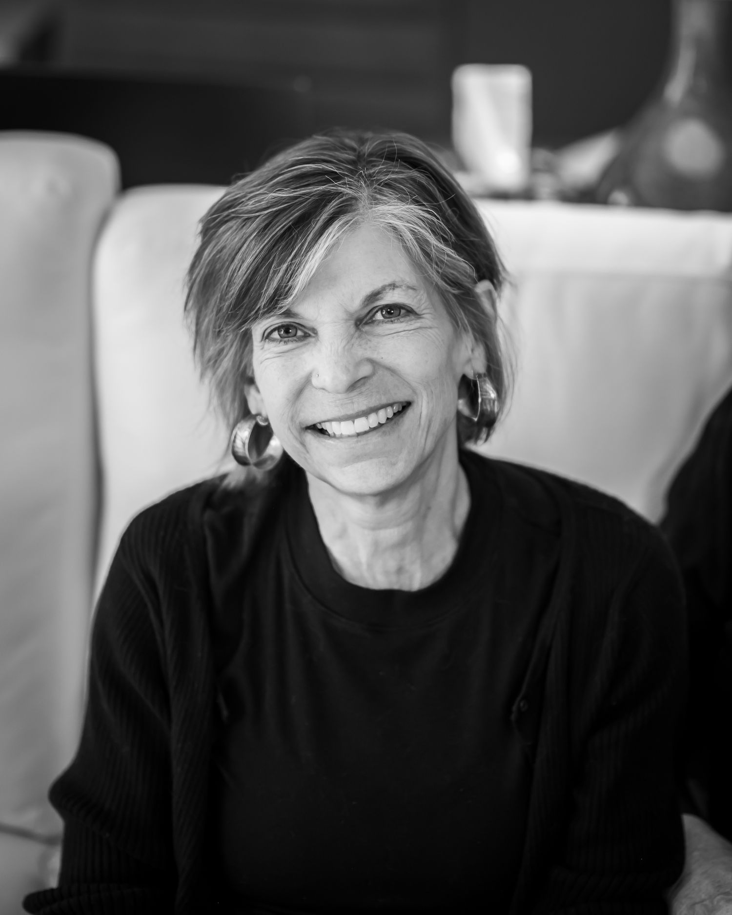 Smiling older woman with short hair wearing a black sweater and hoop earrings in a black and white portrait photo.