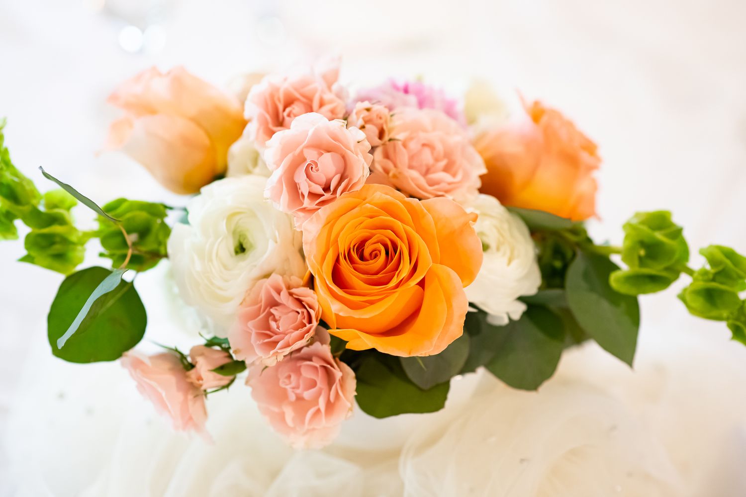 Elegant bouquet of orange, pink, and white roses with green leaves in a white vase.
