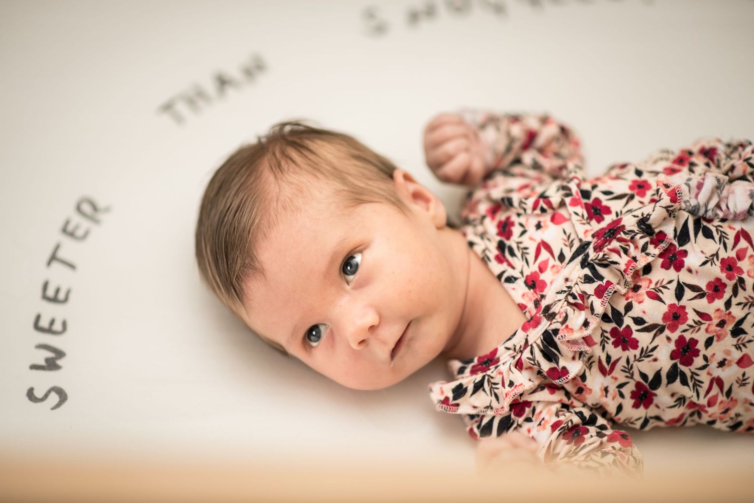 A baby lies on cream-colored fabric wearing a floral print outfit in a series of connected portrait photos.