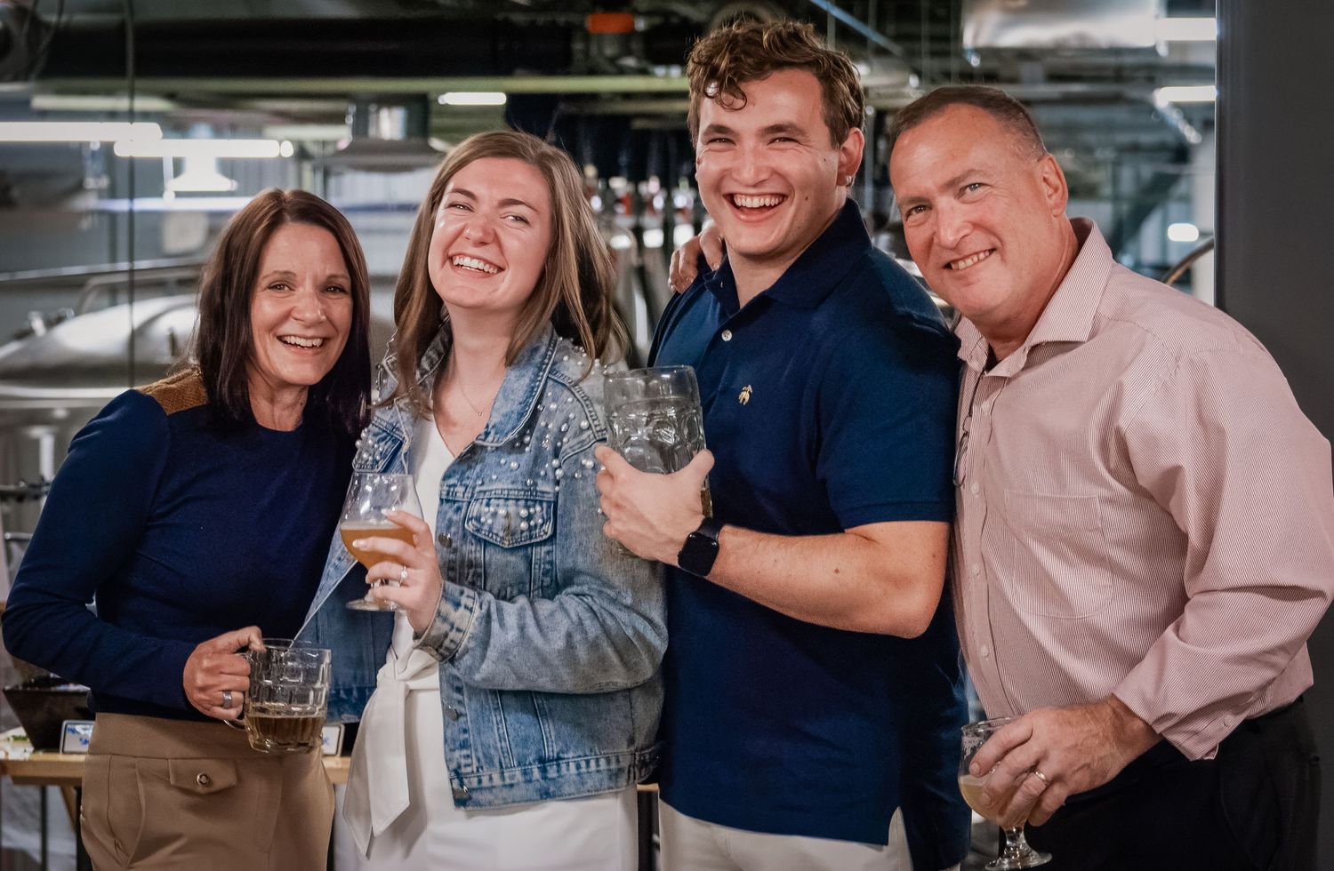 A group of people laughing and socializing while holding drinks at a casual indoor gathering.