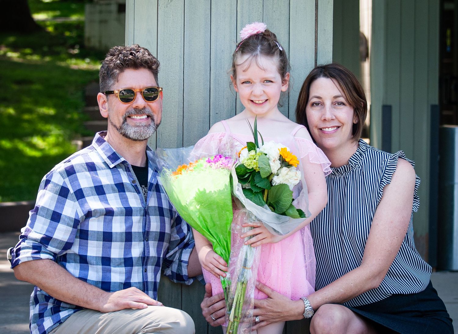 Family poses together outdoors holding a bouquet of flowers on a sunny day.