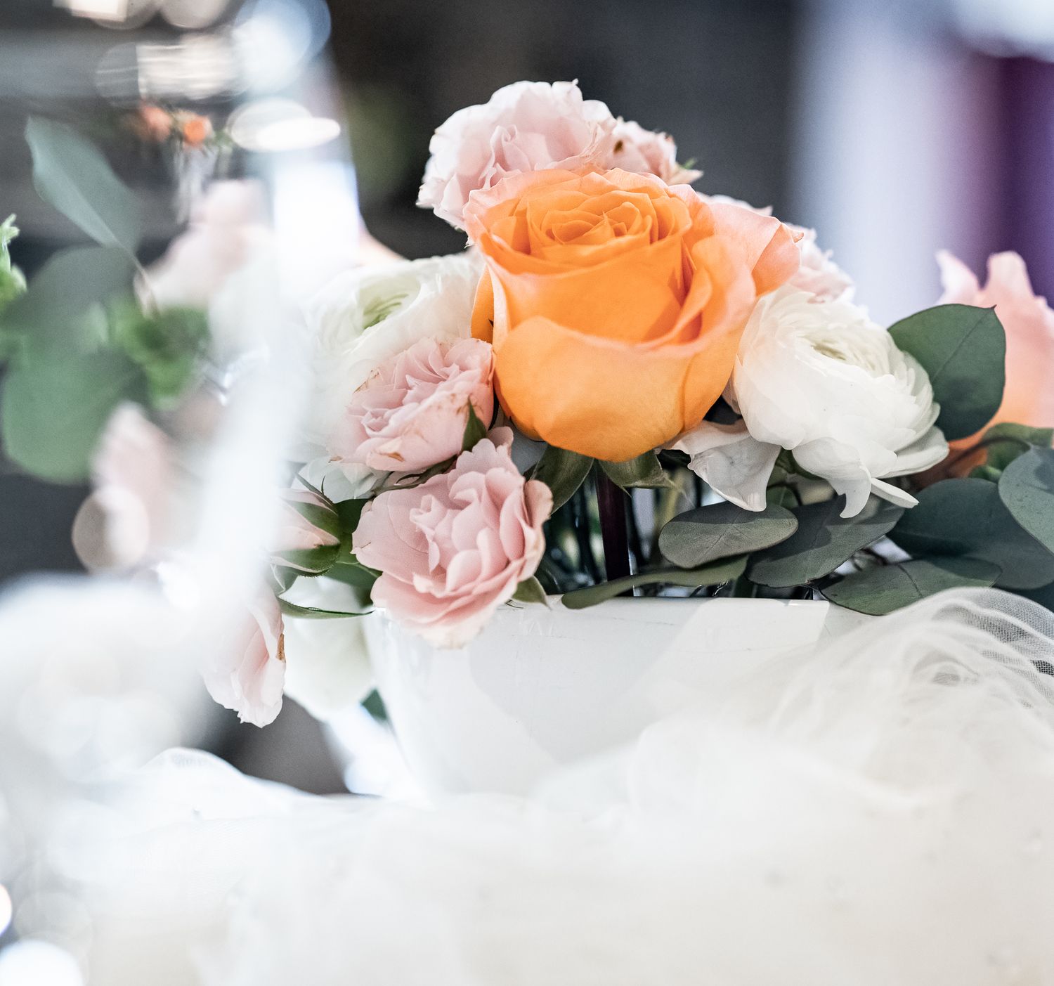 Elegant wedding centerpiece with peach, pink, and white roses in a white bowl vase with eucalyptus greenery.
