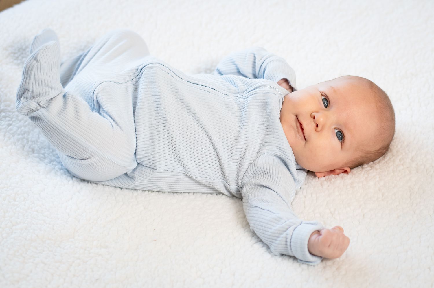 Baby wearing light blue onesie lying on white blanket in sequence of rolling over poses.