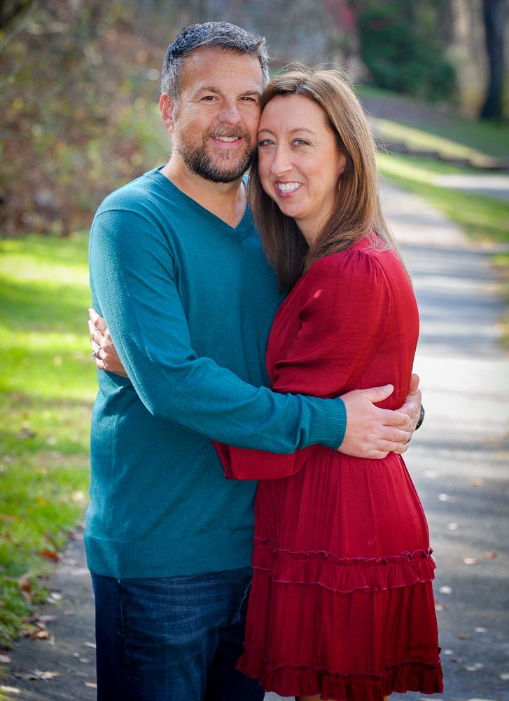 A couple embraces outdoors on a tree-lined path during an autumn engagement photo session.