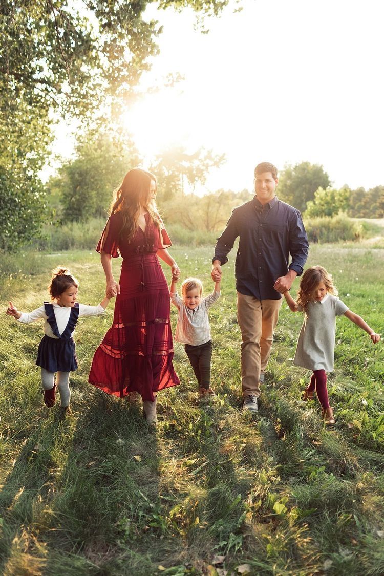 A family walks together through a sunlit field at golden hour holding hands and enjoying nature.