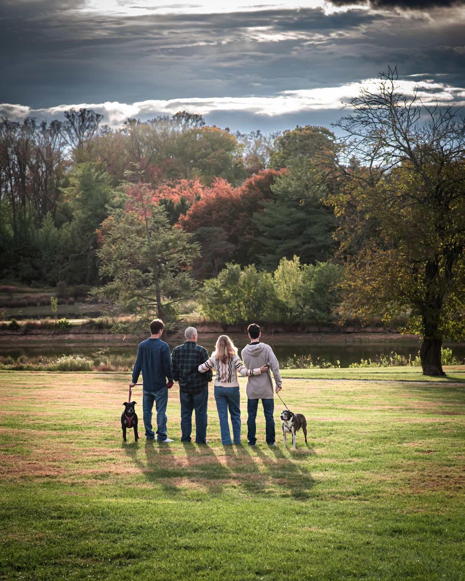Family and dogs standing together in a grassy field on an autumn day with dramatic clouds overhead.