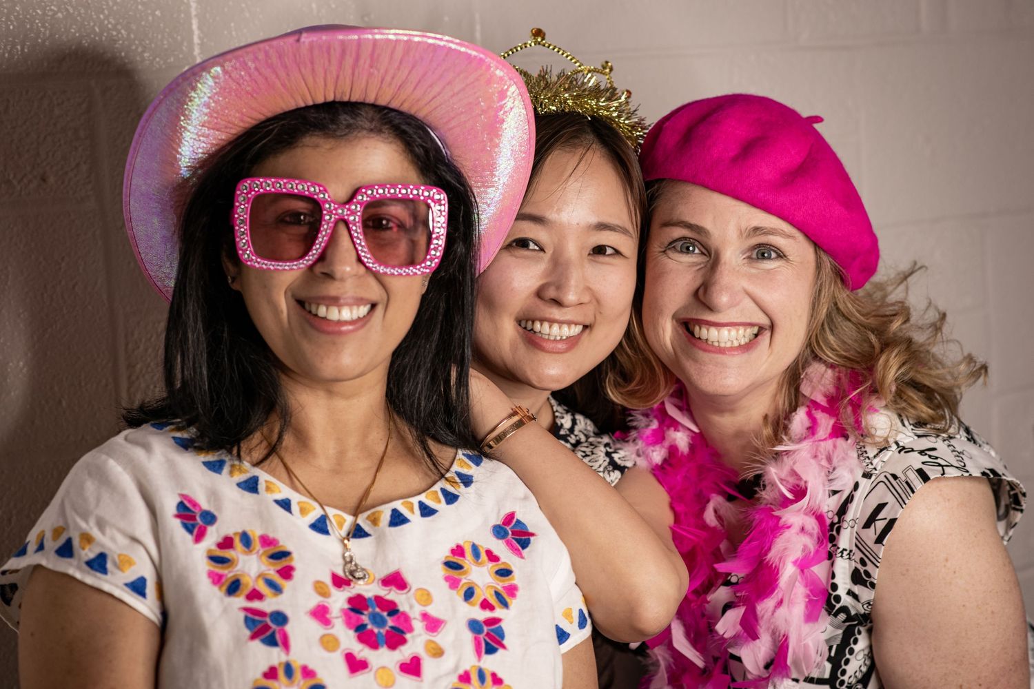 A group wearing pink hats and festive party accessories poses together for a celebratory photo.
