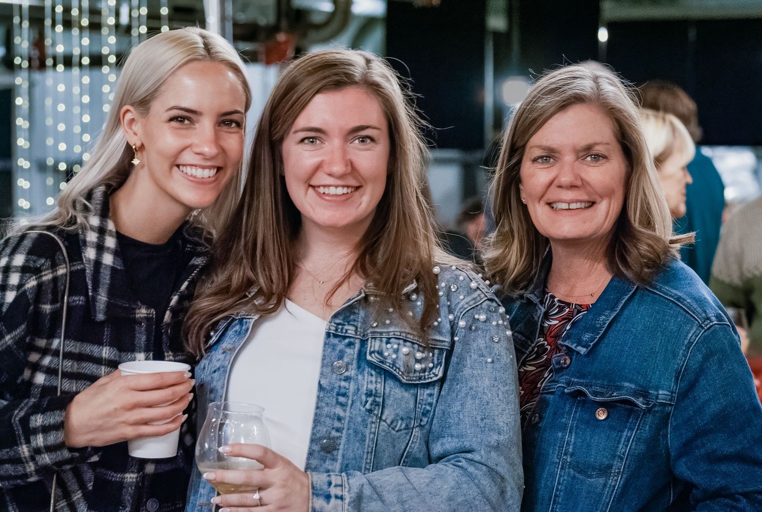 Group of friends in denim jackets smiling and enjoying beverages together outdoors.