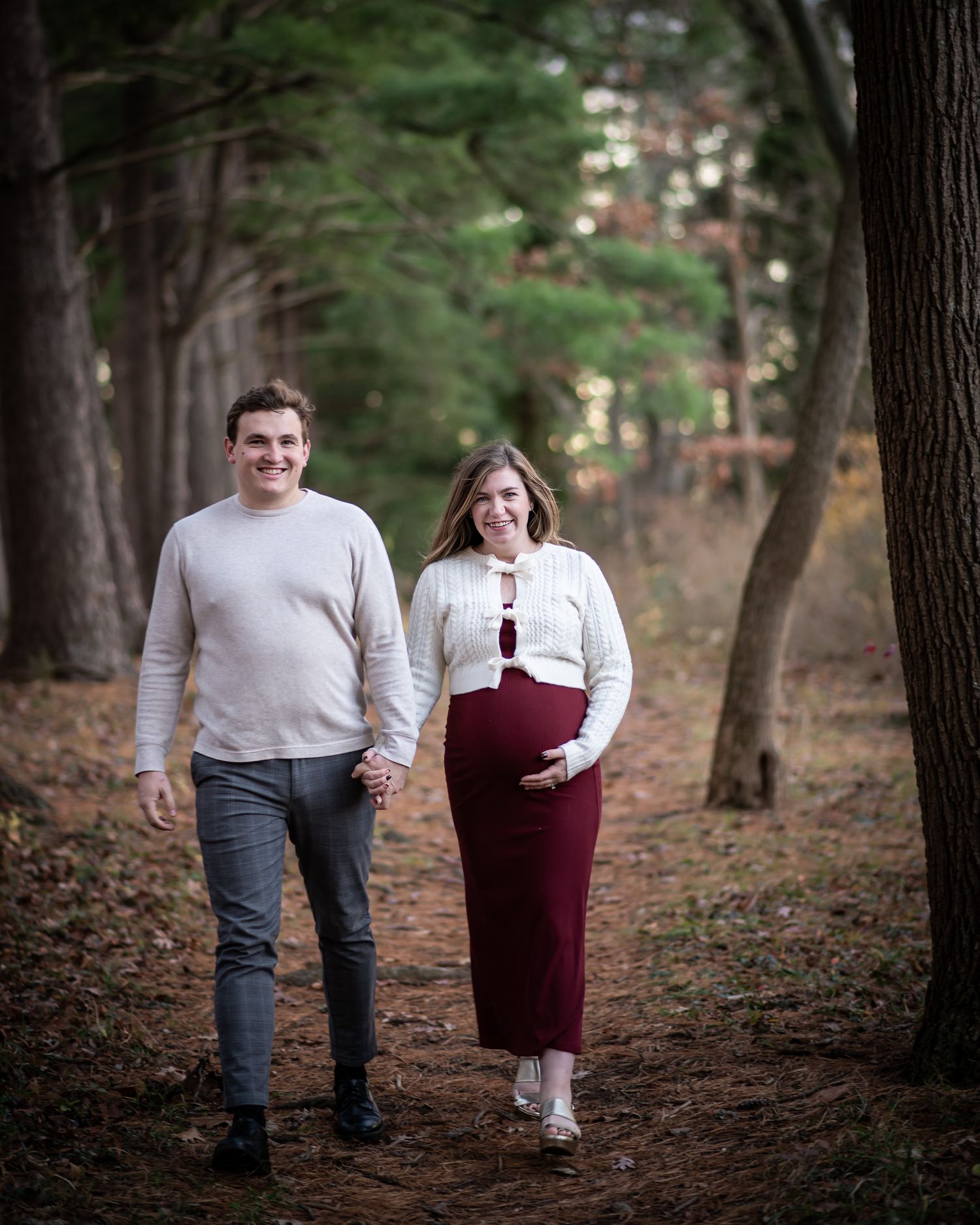 A couple walking together through a wooded path covered in fallen leaves on an autumn day.