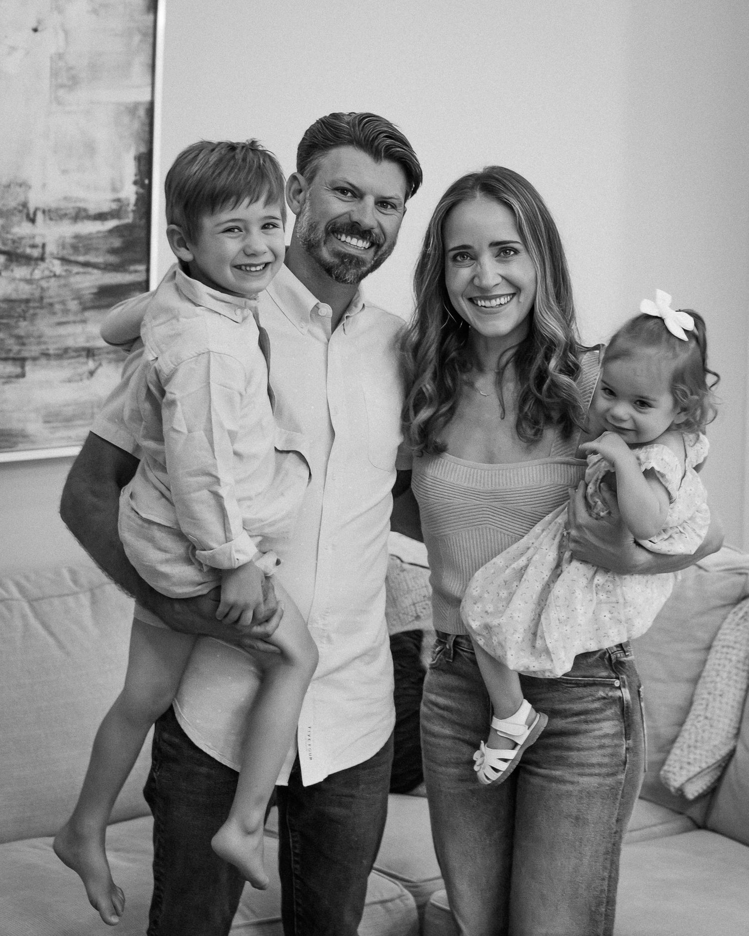 Black and white family portrait of smiling parents holding two young children indoors.