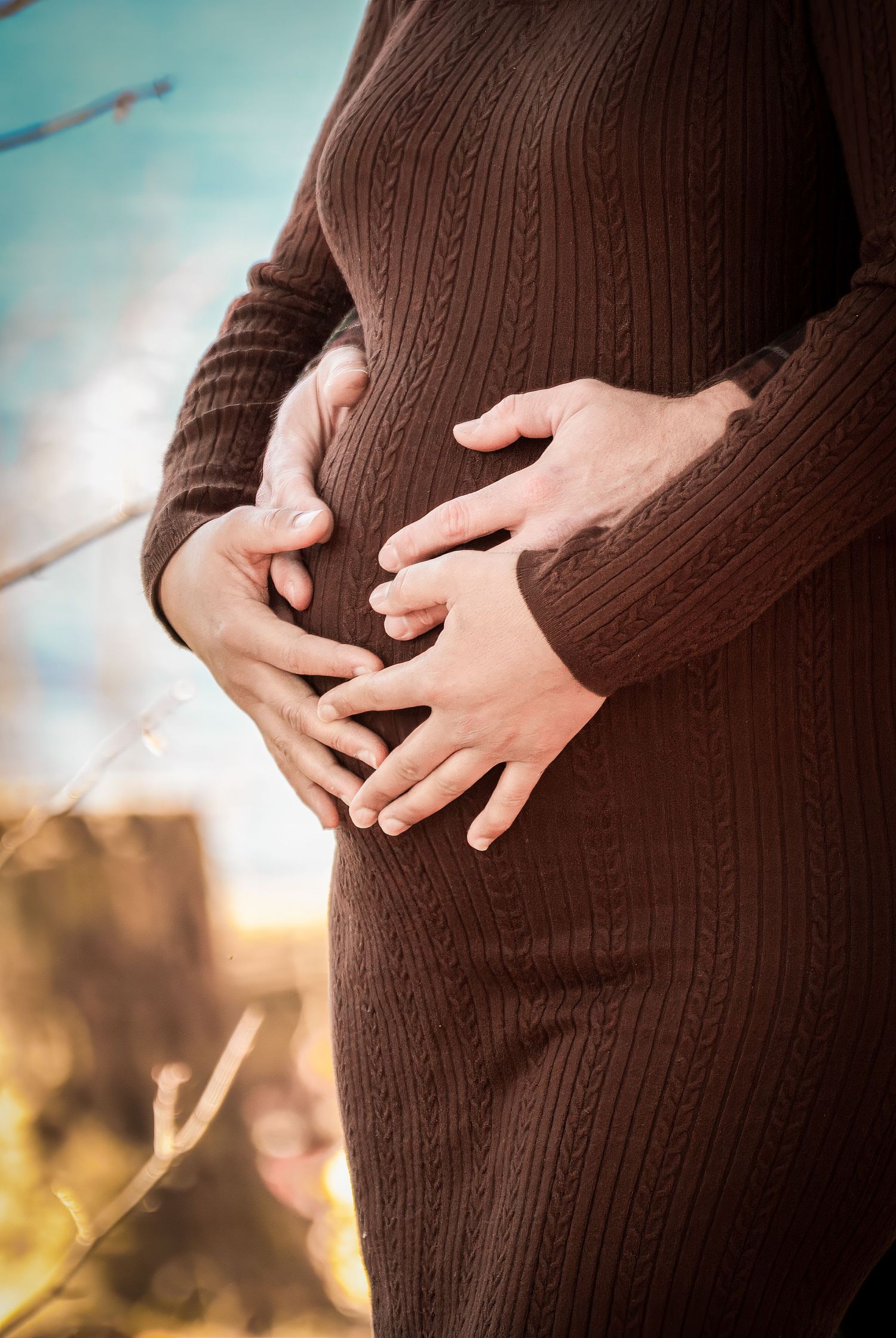 Close-up sequence showing hands gently cradling a pregnant belly in a brown sweater against a soft blurred background.