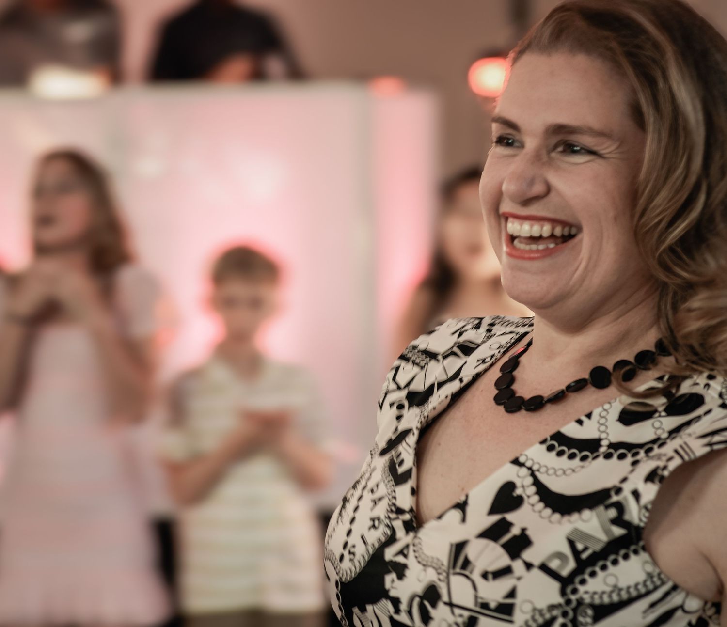 A joyful moment captured at a celebration with people laughing and enjoying themselves in a warm pink-lit atmosphere.