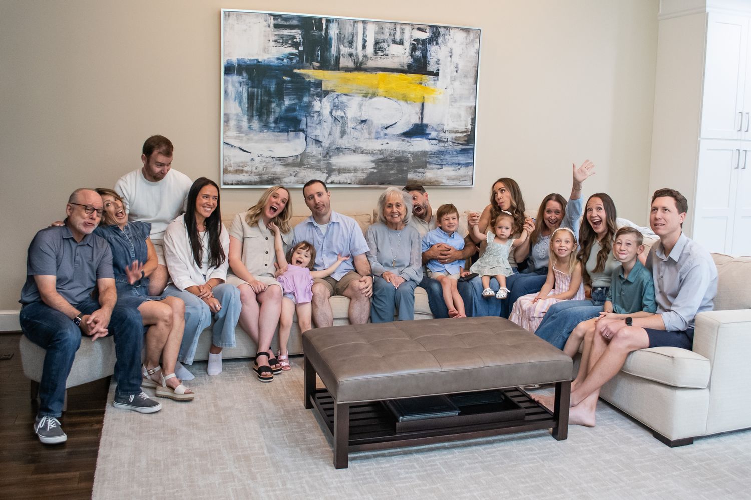 Large multigenerational family smiling together on a couch in a bright modern living room for a portrait photo.