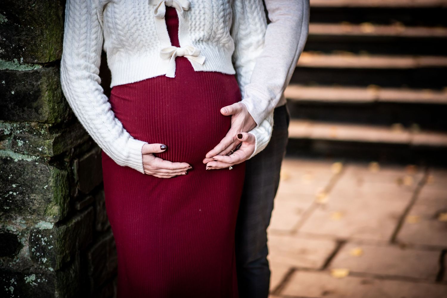 A couple in burgundy and white attire embraces while standing outdoors on stone steps.