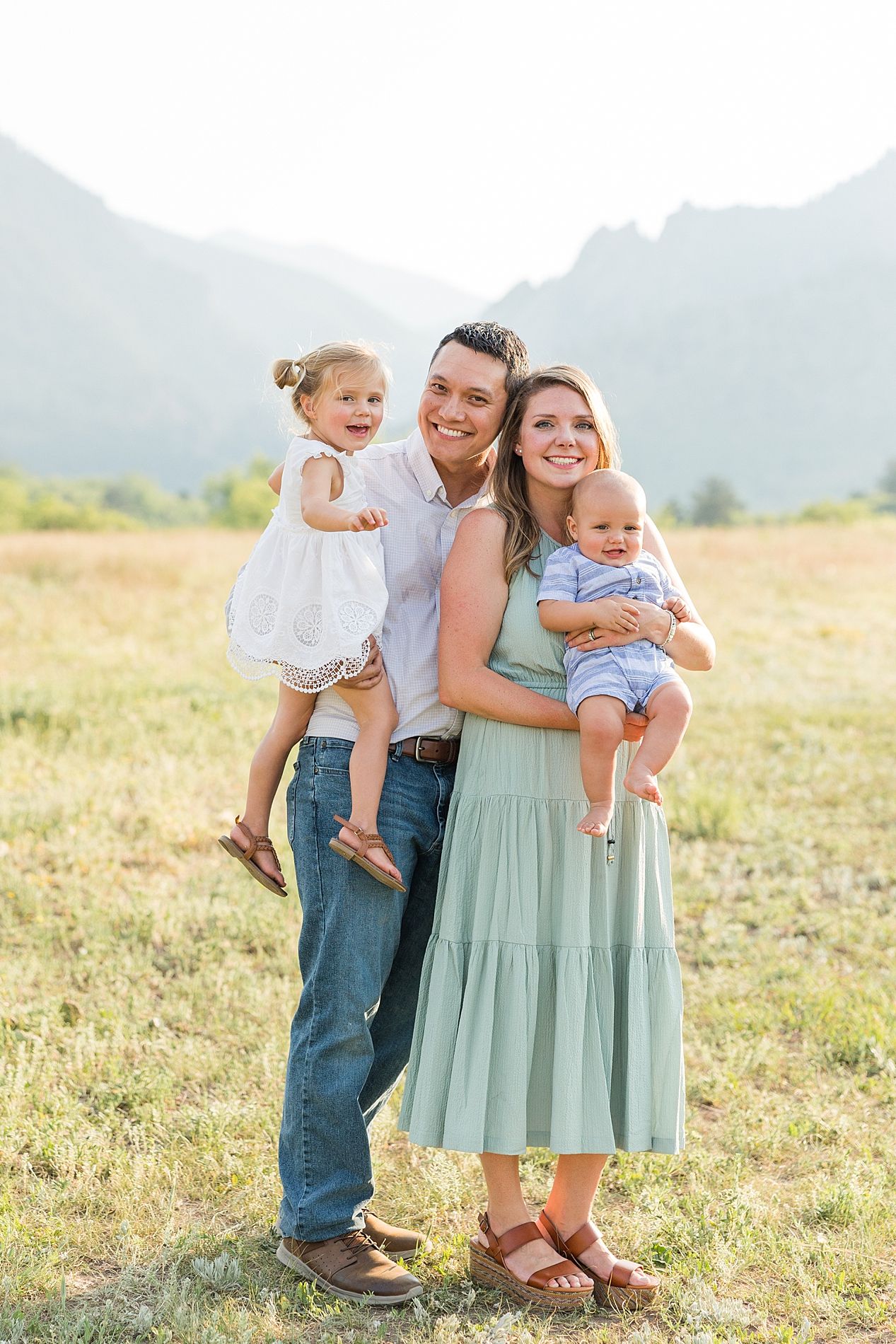 A family stands together in a grassy field with mountains visible in the background on a sunny day.