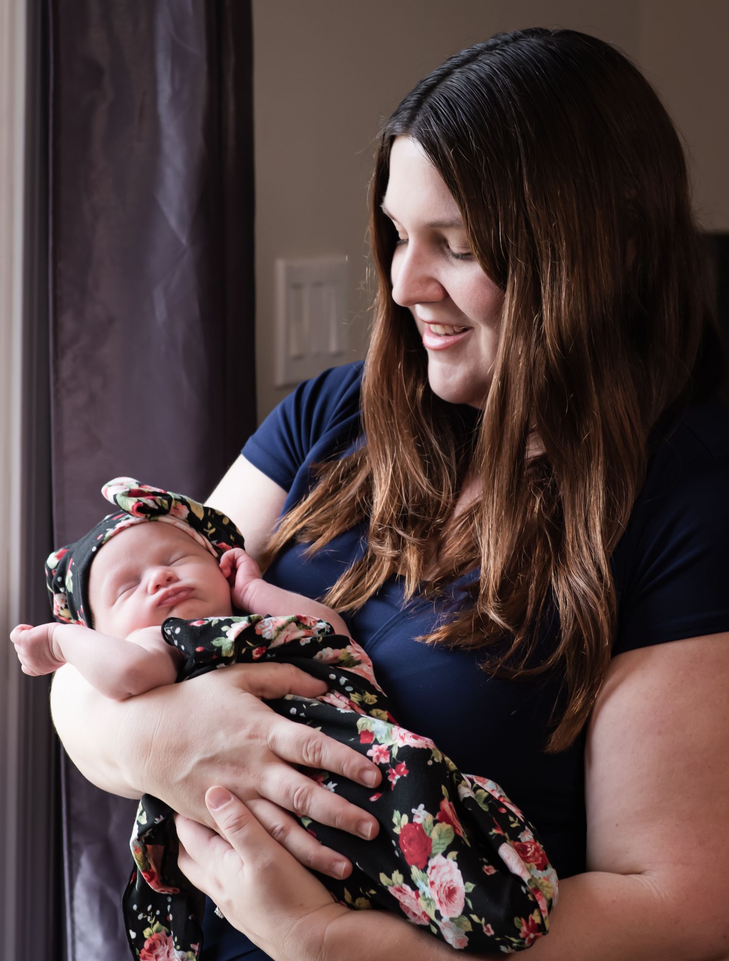 A tender moment between a parent and newborn wearing a floral outfit by a window.