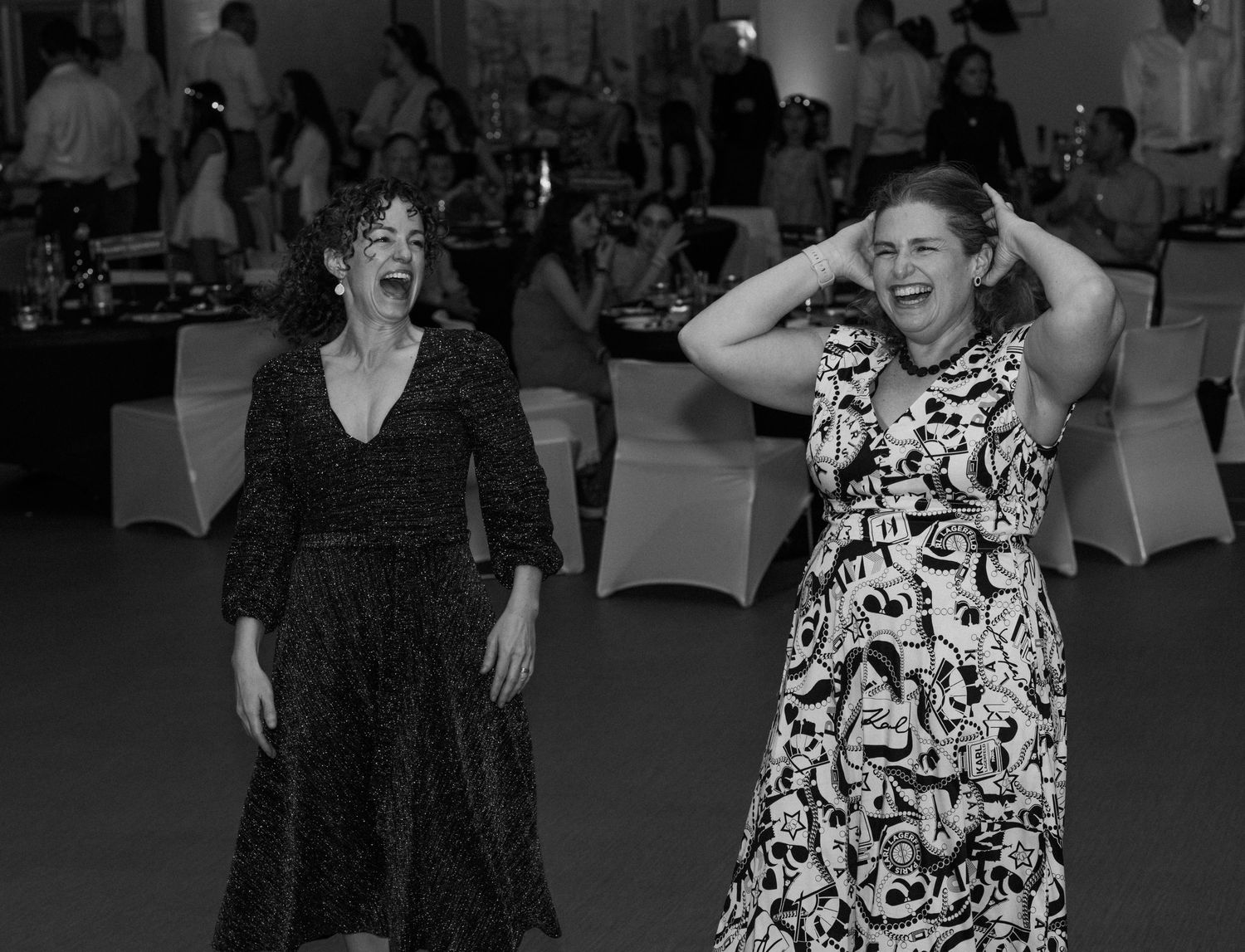 Two people in dresses dancing and having fun at a formal event captured in black and white photography.