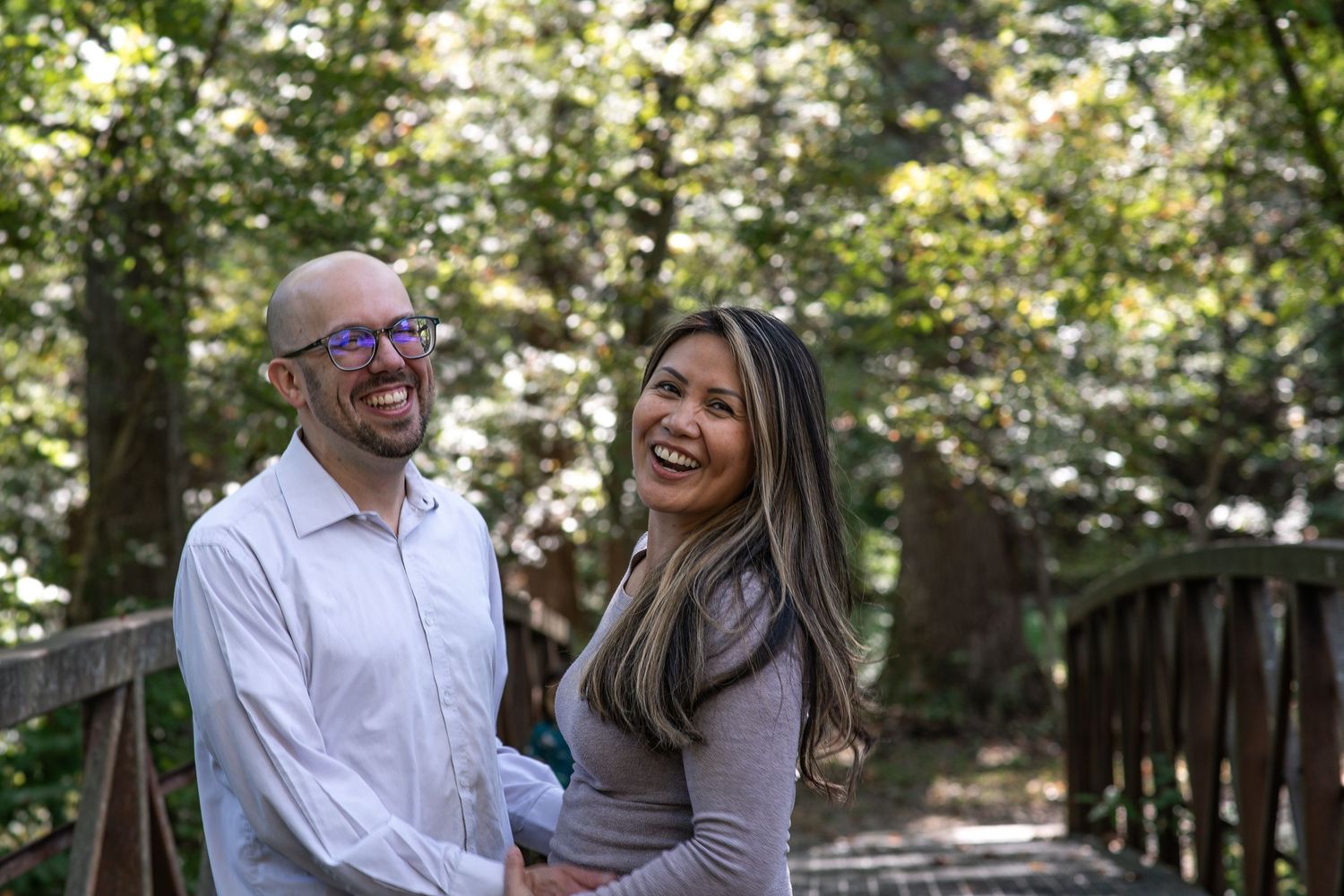 Happy couple smiling on a wooden bridge surrounded by lush green forest trees.
