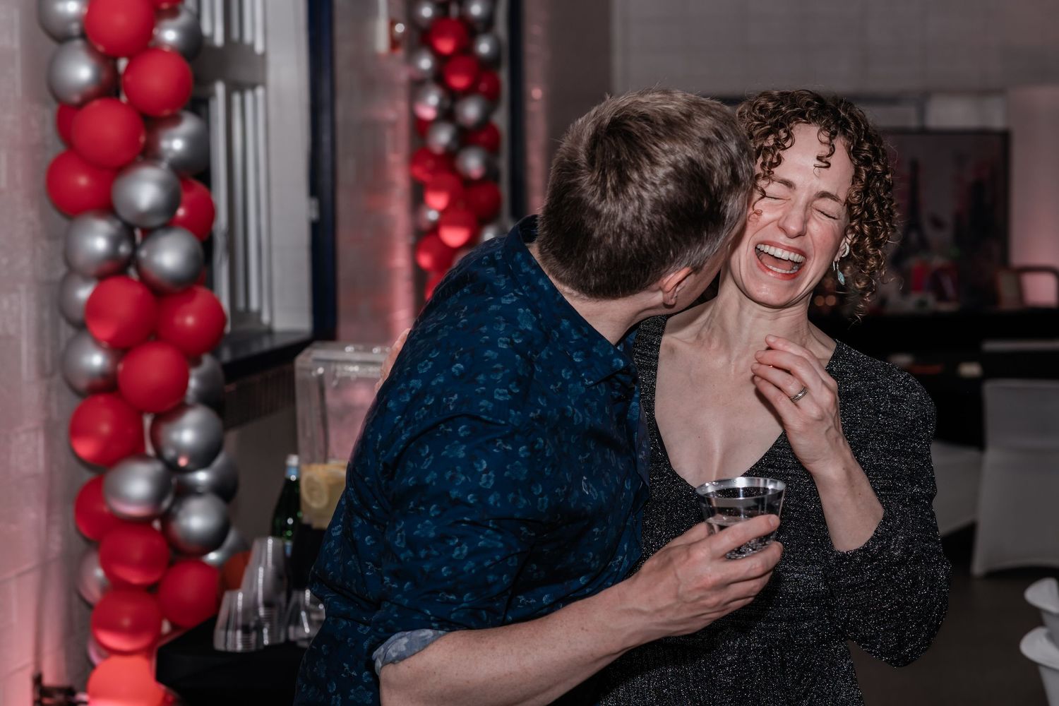 Group of people celebrating at an event with red and silver balloon decorations in the background.
