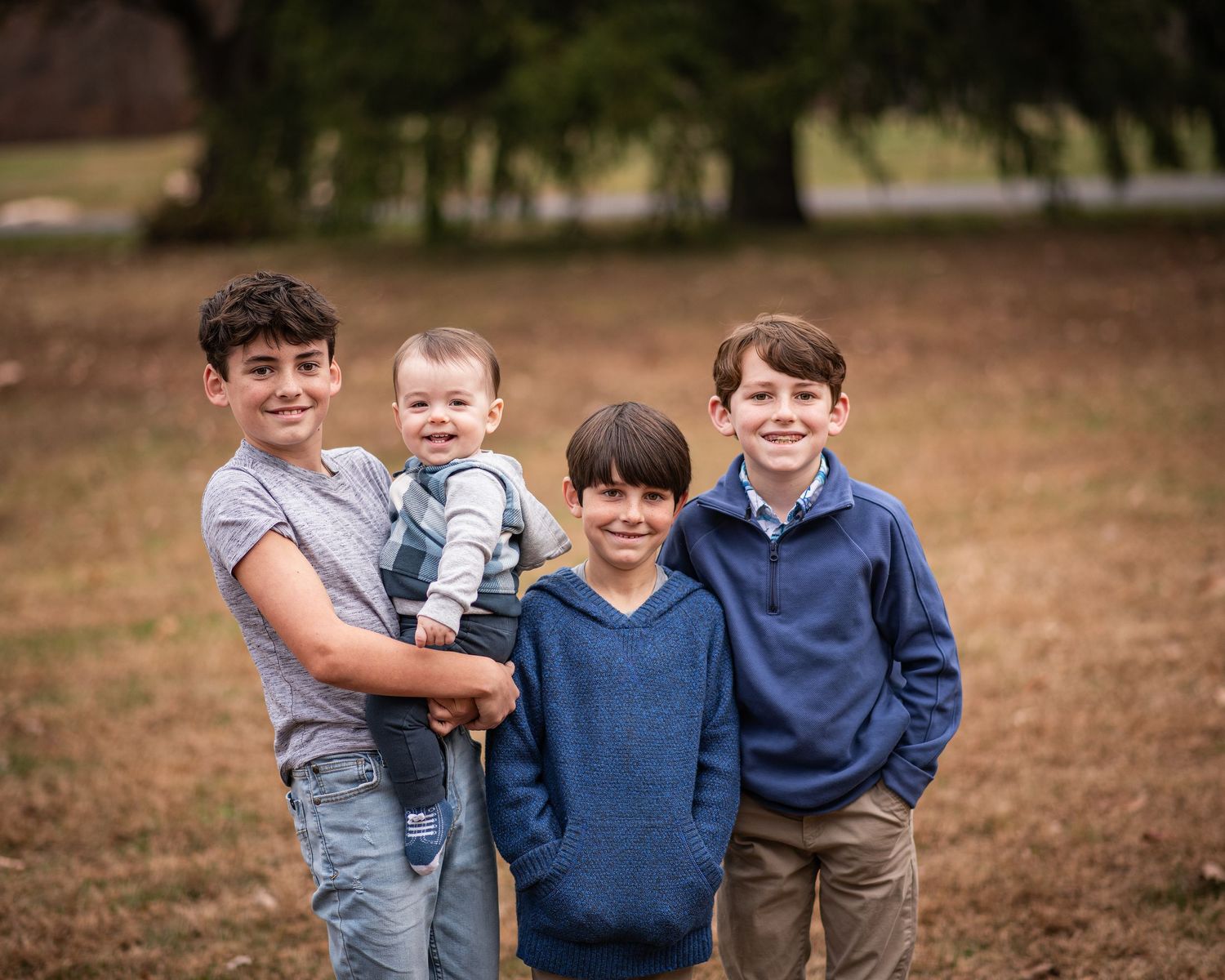 A group of people wearing blue sweaters and casual attire pose together outdoors in a natural setting.