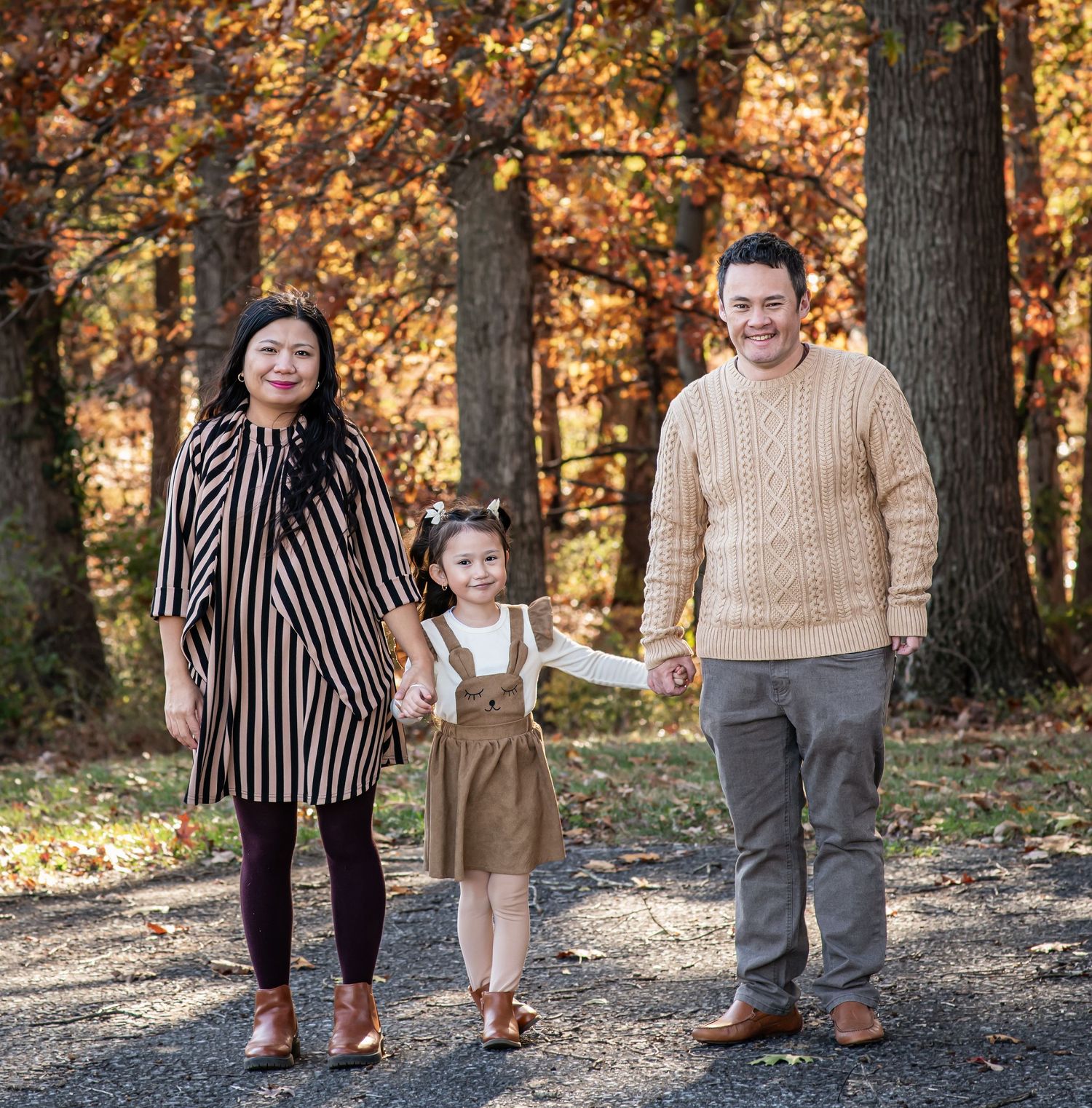 A group stands on a leaf-covered path in autumn woods with warm golden sunlight filtering through the trees.