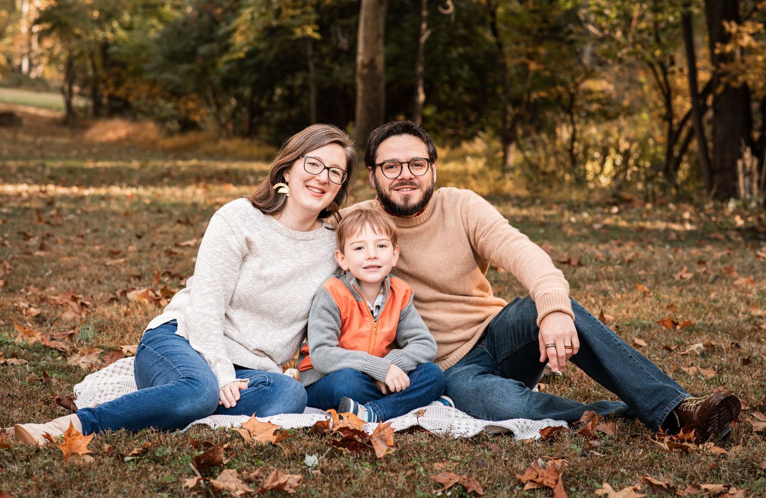 A family relaxes together on autumn leaves during a fall photo session in a park setting.