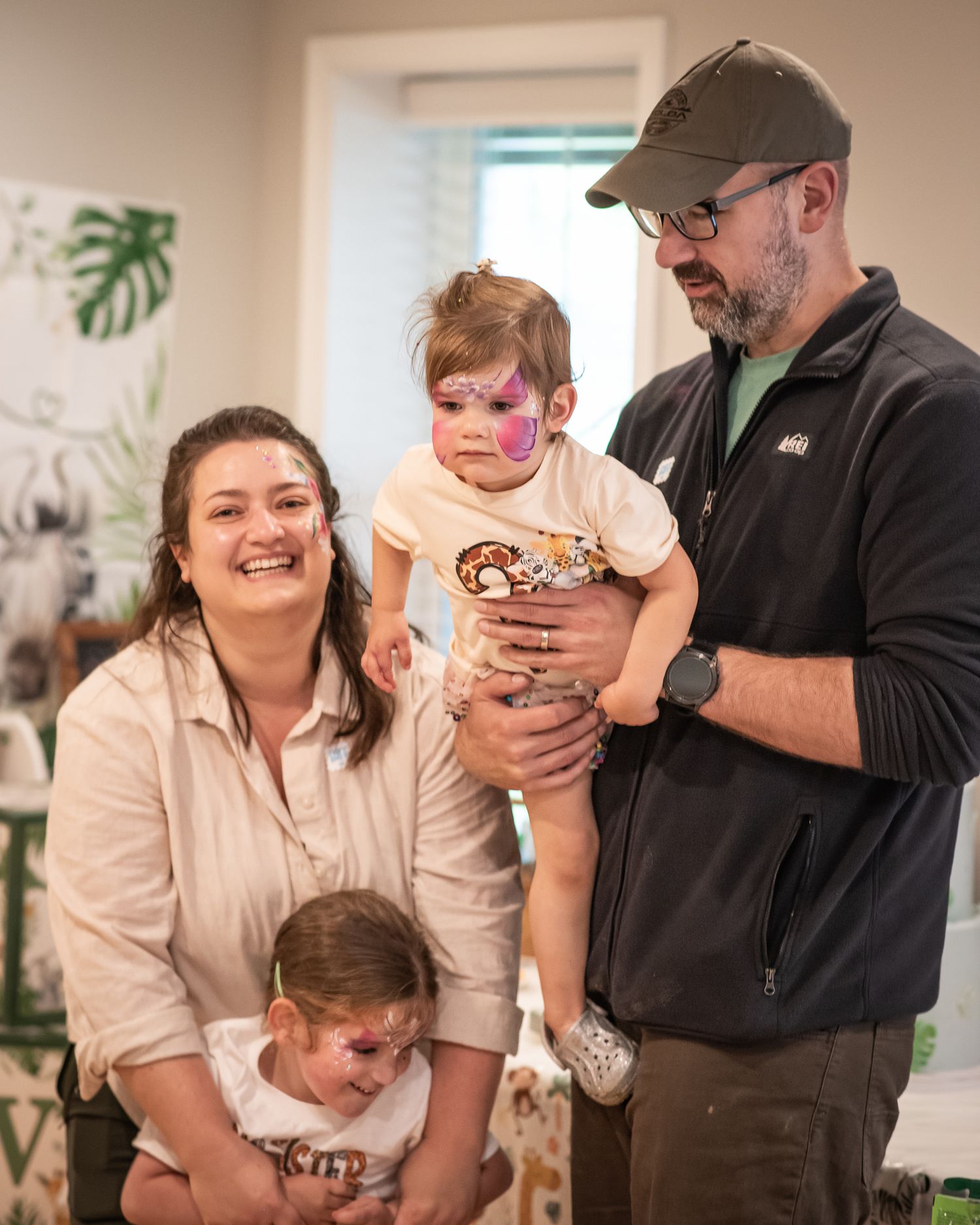 Happy family with face-painted children smiling together at a birthday party celebration indoors.