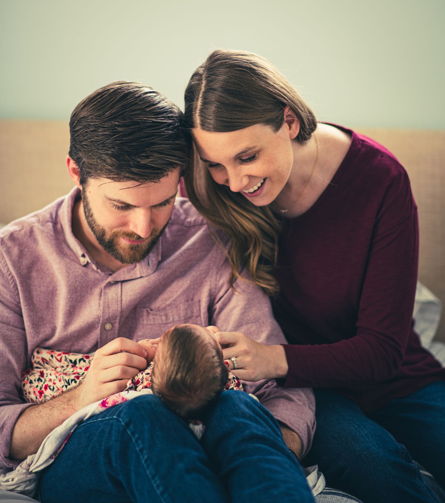 A couple sits together on a couch while tenderly looking down at their baby in a series of intimate family moments.