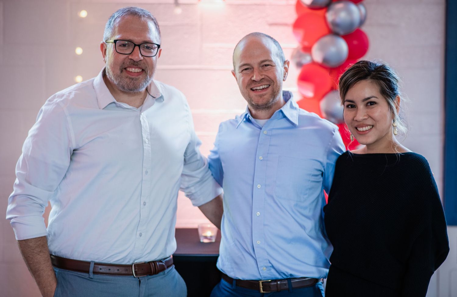 Professional gathering with people in business attire standing together against a backdrop with balloons.