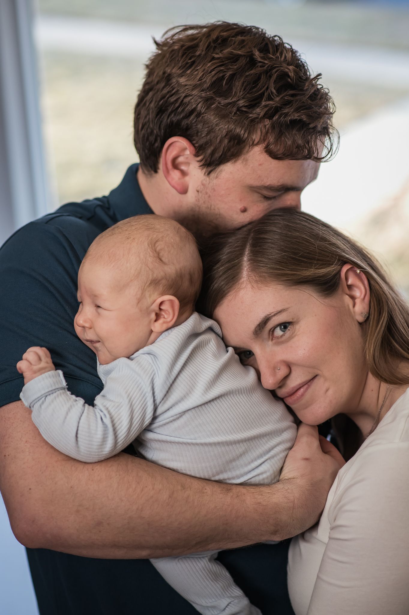 A young couple tenderly embracing their newborn baby, sharing a loving family moment together.