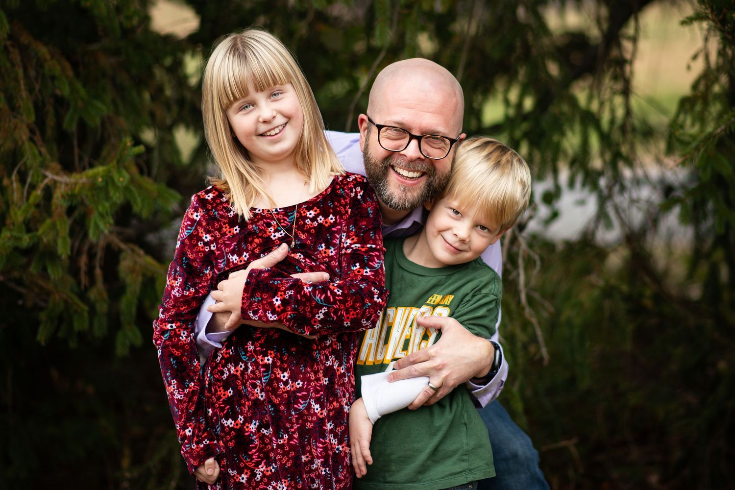 A family poses together in an outdoor setting with evergreen trees in the background.