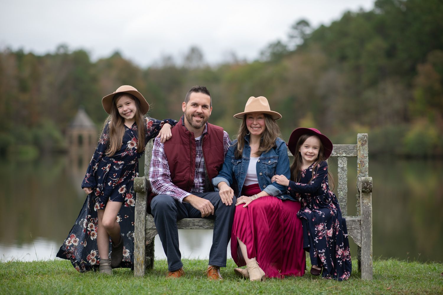 A family sits together on grass near a lake during an outdoor photo session.