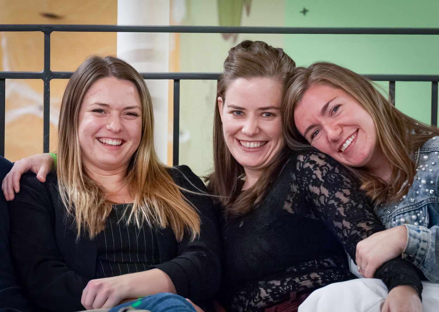 Three friends wearing black tops smile together while sitting close and enjoying each other's company.