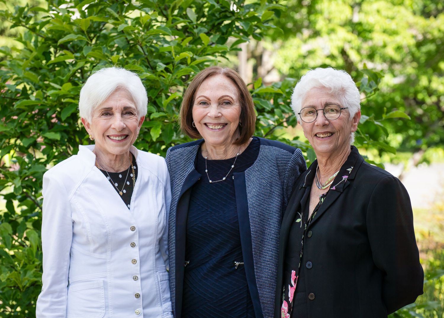 Group of people smiling and posing together outdoors in a garden setting on a sunny day.
