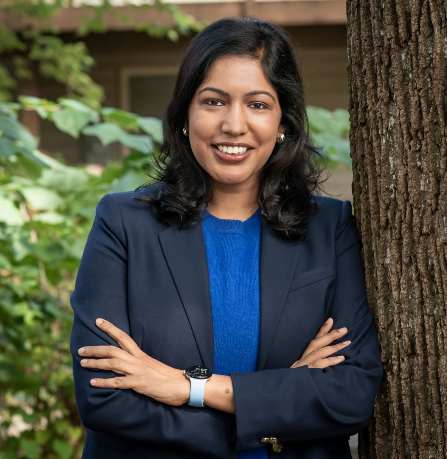 Professional wearing a navy blazer and royal blue top poses confidently against trees in an outdoor setting.