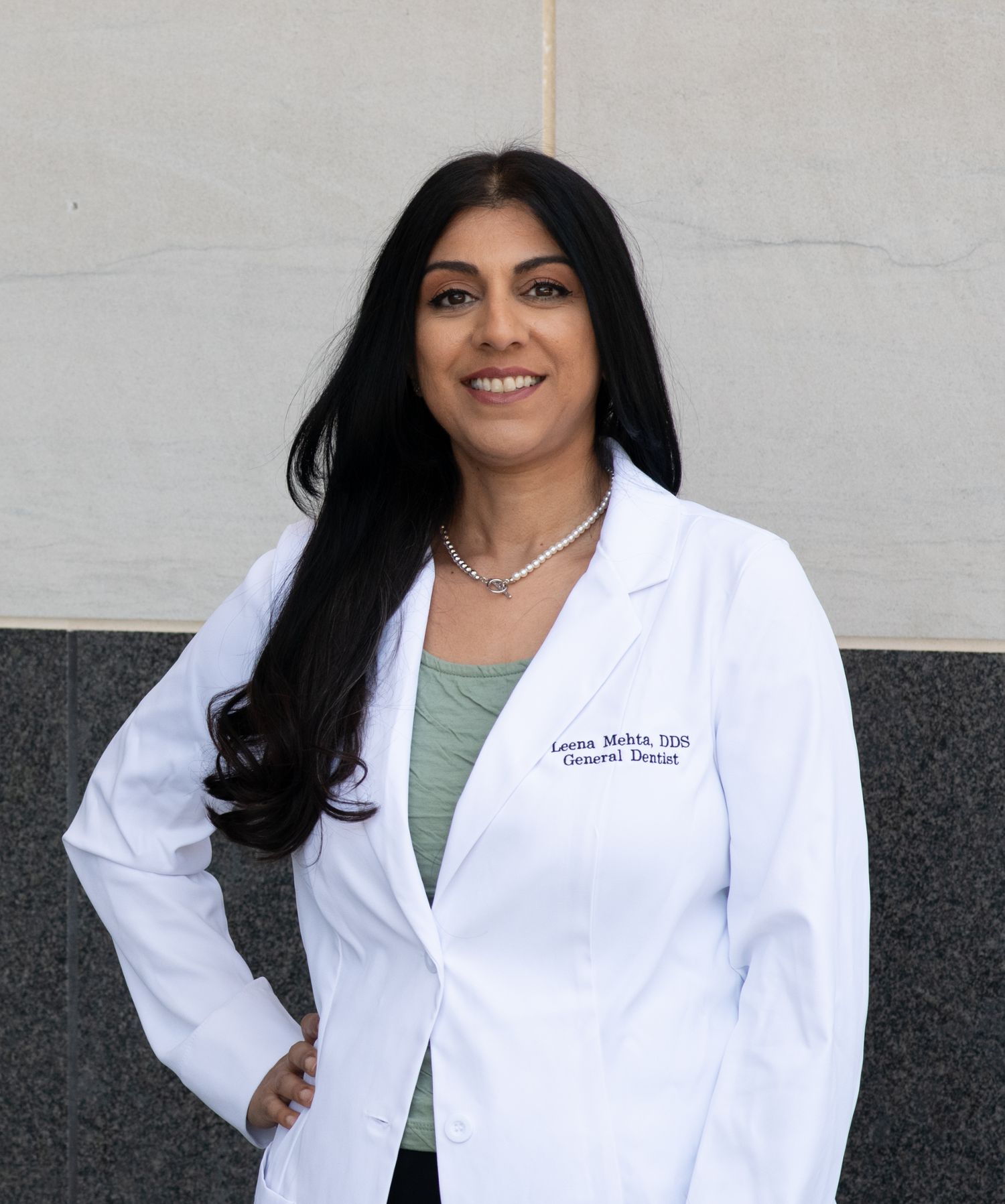 Medical professional in a white lab coat and green top poses against a gray background.