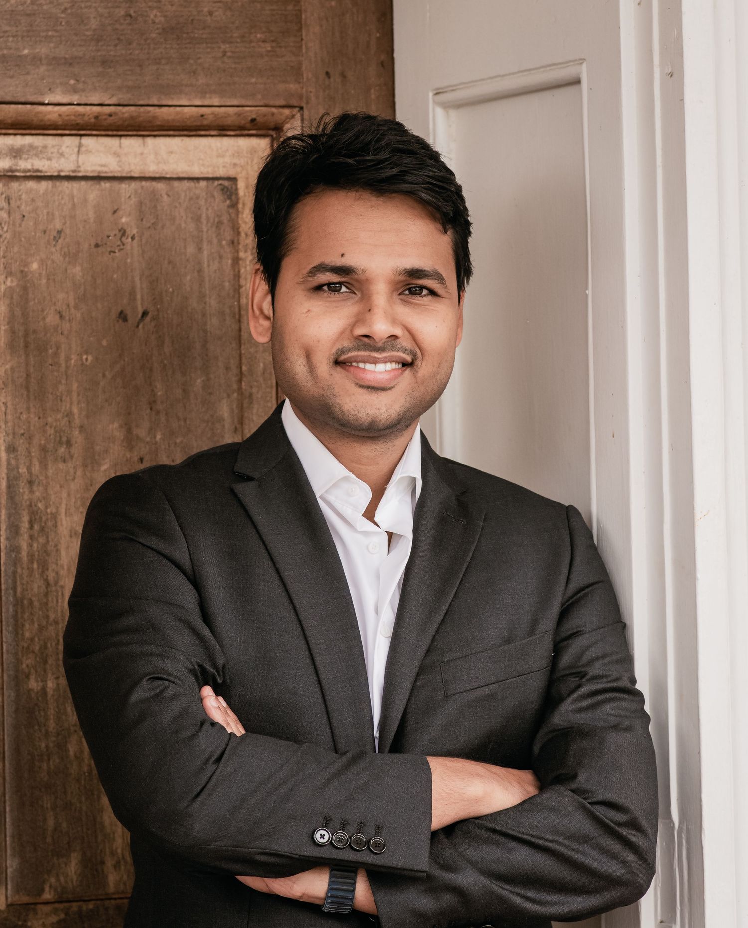 Professional wearing a dark suit and white shirt poses confidently against a neutral background.
