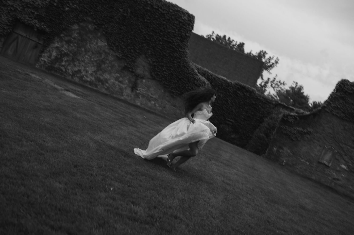 Child in white dress and black hat twirling in a garden, black and white photography.