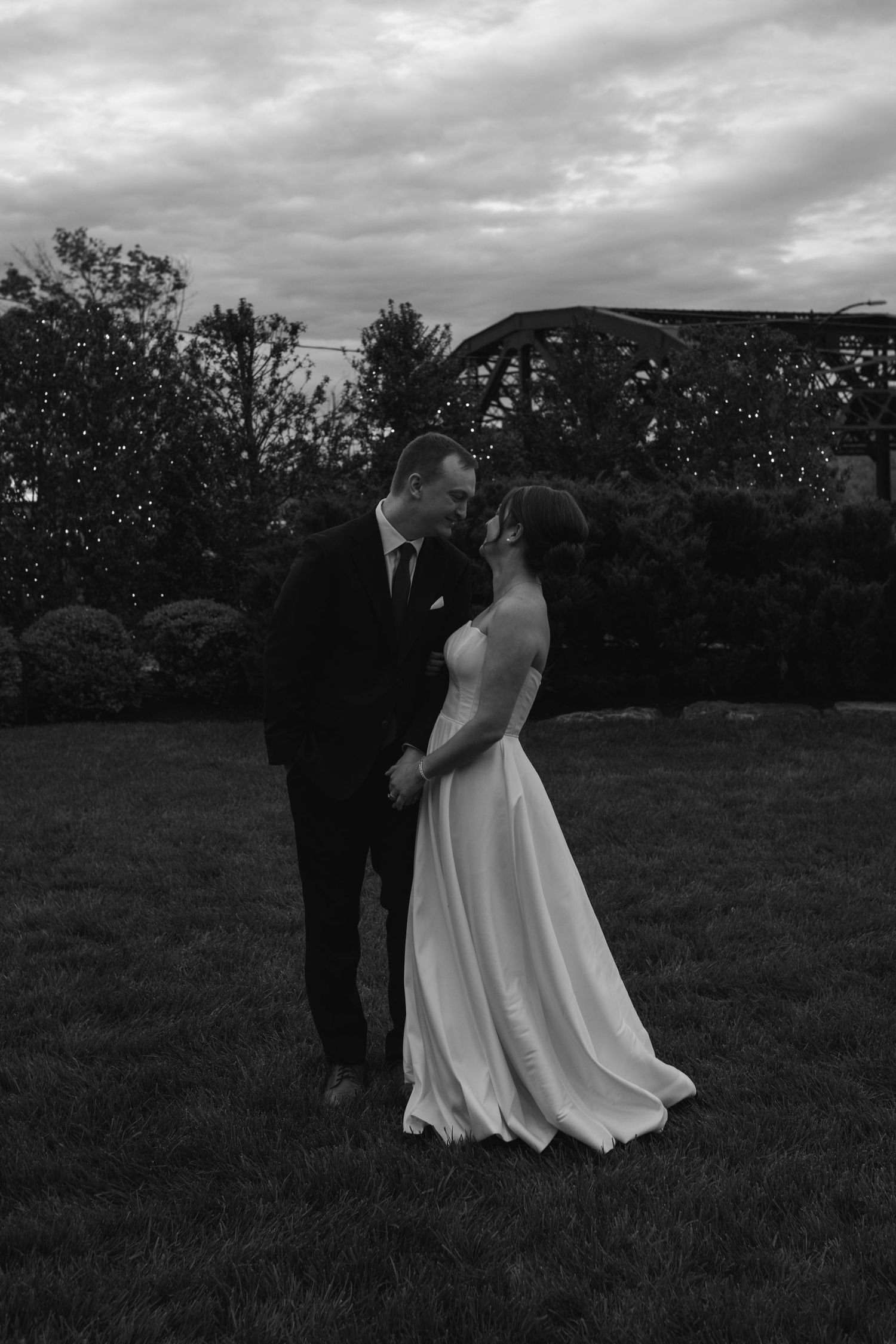 Black and white photo of a bride and groom holding hands and sharing a romantic moment outdoors at dusk.