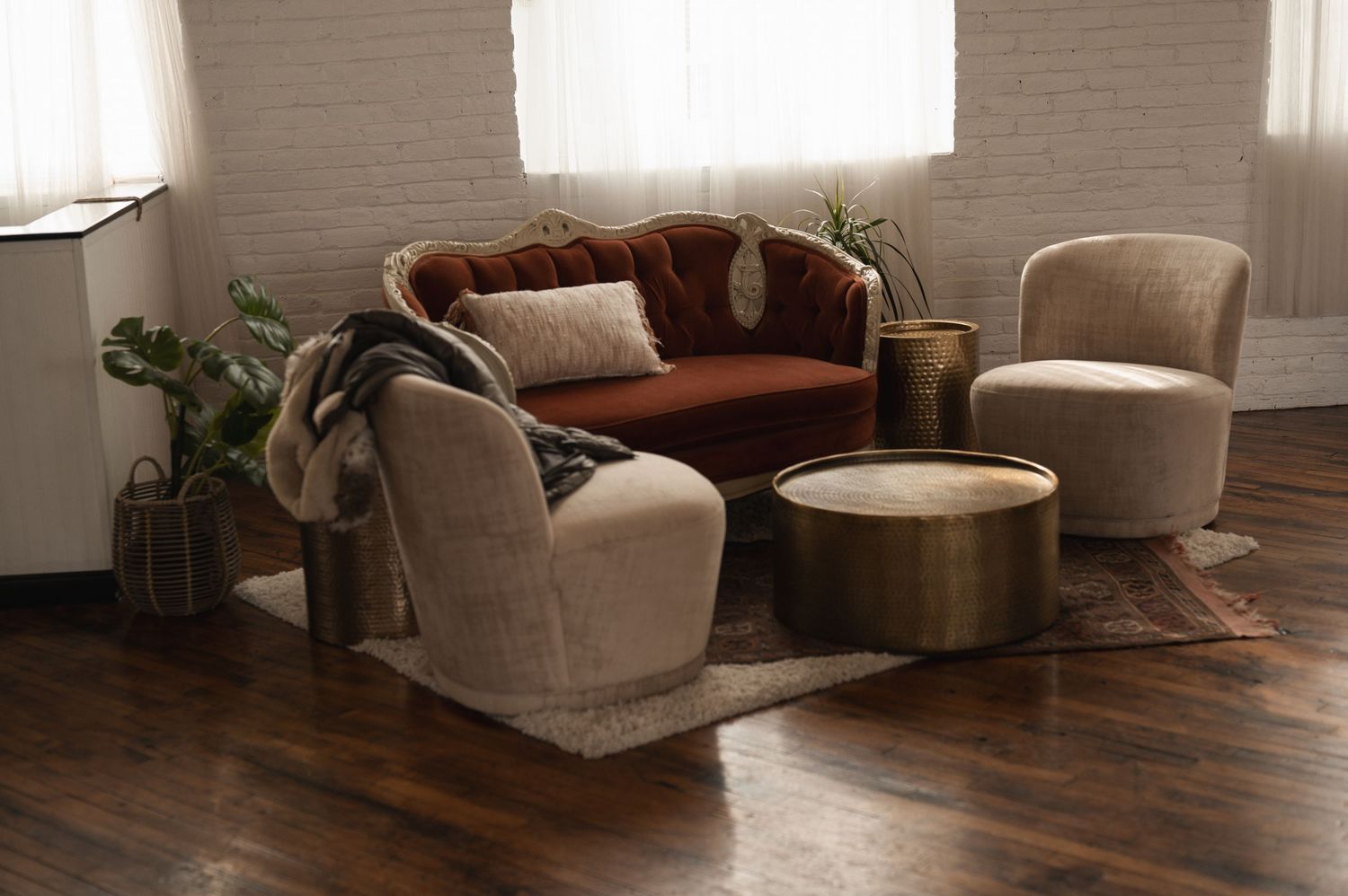 Modern living room interior with white sofa, dark hardwood floors, and natural light streaming through windows.