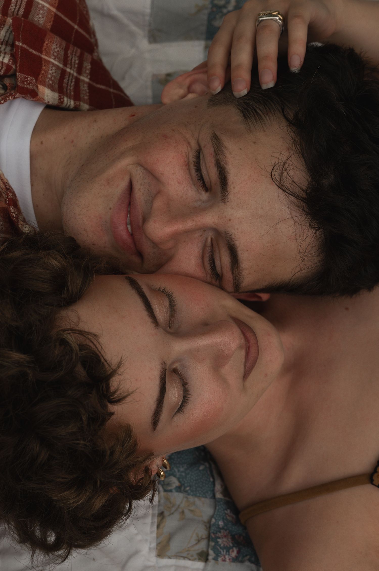 Two people lying close together with eyes closed, smiling peacefully, in an intimate and tender moment.