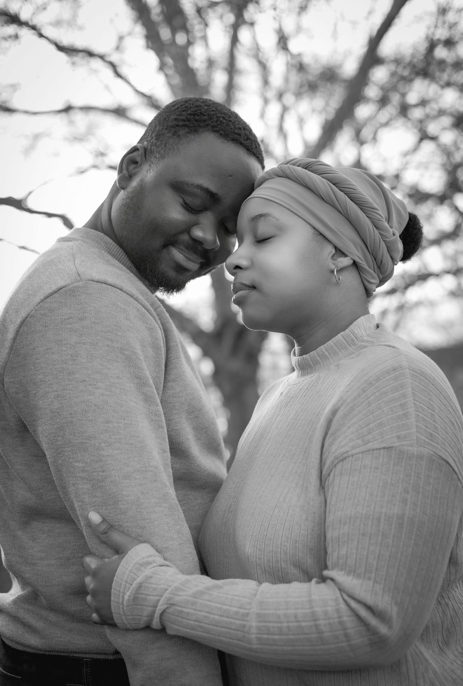 Black and white photo of a couple embracing tenderly, foreheads touching, with trees in the background.
