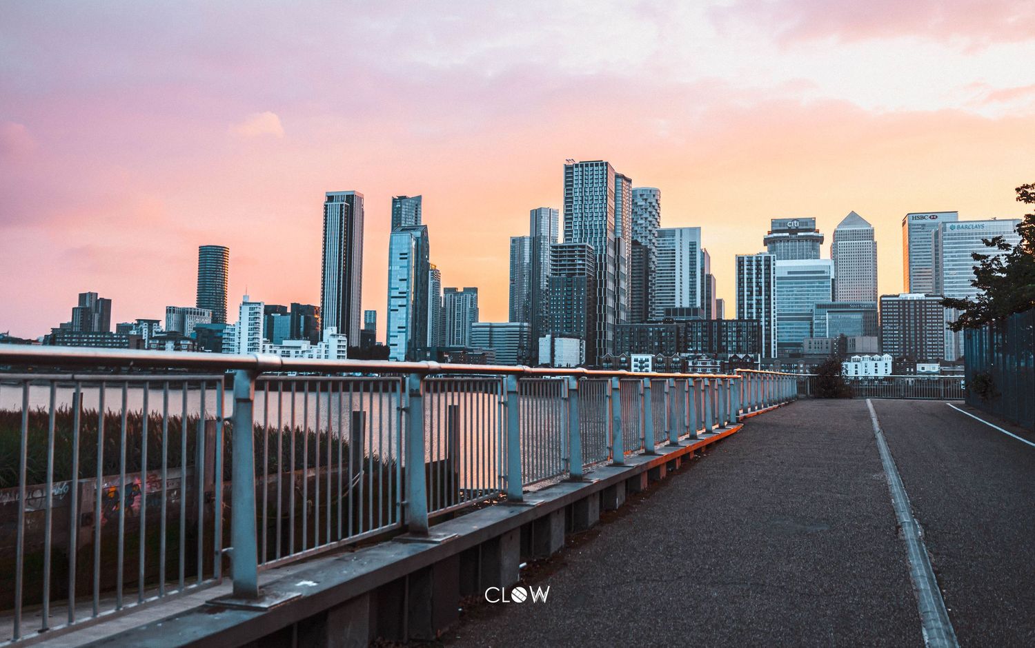 Scenic cityscape view of downtown skyscrapers at sunset from a waterfront boardwalk with pink and orange sky.