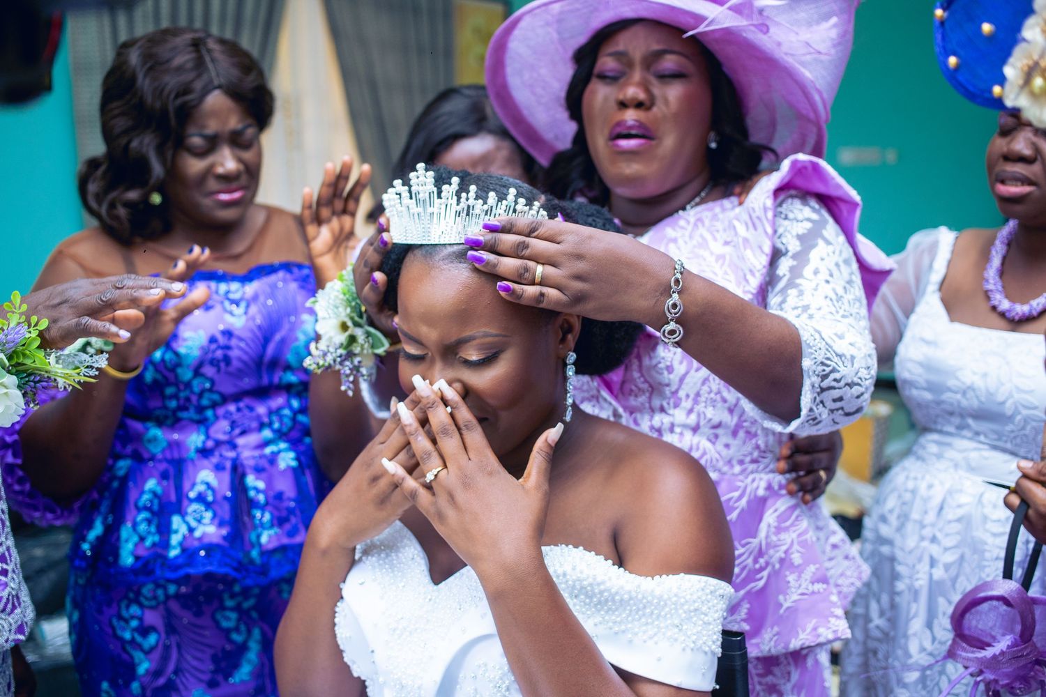 A touching moment during a wedding ceremony as a crown is placed on someone wearing a white dress while guests look on.
